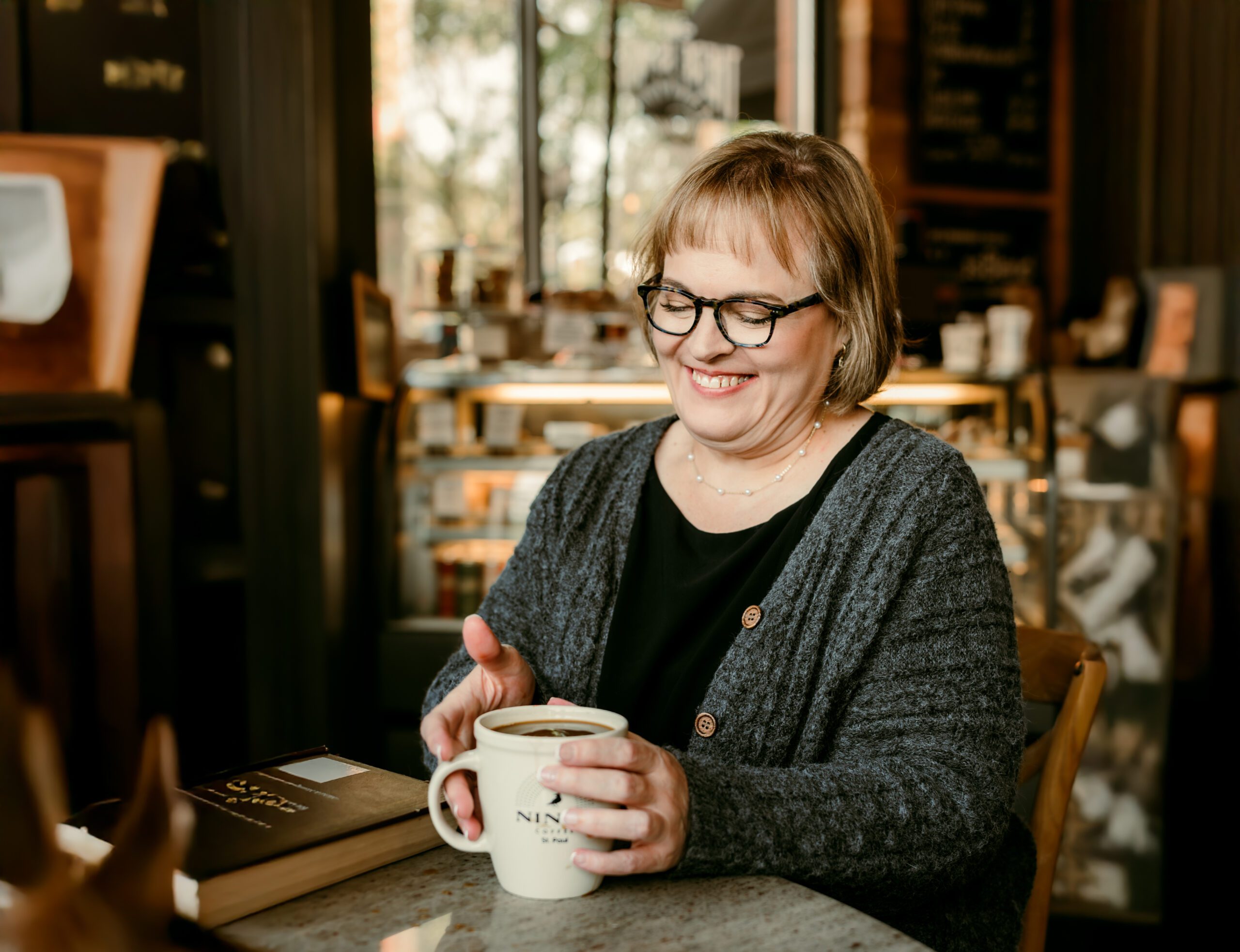 Smiling woman holding a coffee at Nina’s Café in St. Paul, showcasing a warm and approachable look for Minneapolis dating photography.